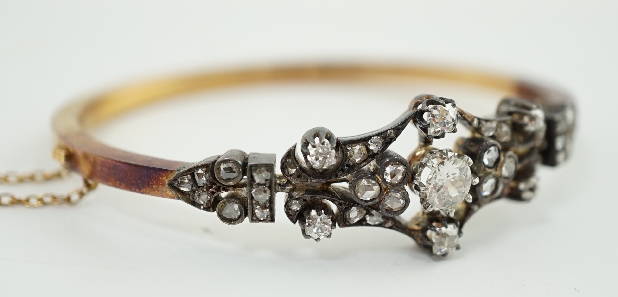 A late 19th/early 20th century French 18ct gold, silver, rose and round cut diamond cluster set hinged bangle